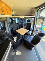 Bright RV rental interior showing versatile seating, a central table, kitchen, and an overhead bed platform.