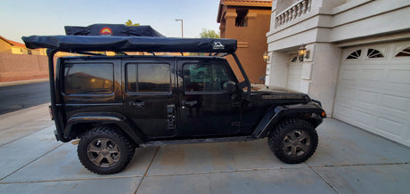 A black Jeep Golden Eagle Wrangler with a rooftop tent and awning system, perfect for an RV rental outdoor escape.