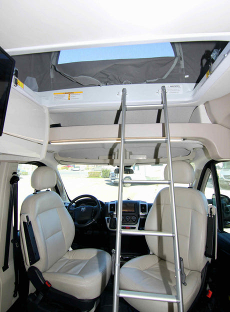 RV rental interior: front cab, dashboard, and a ladder leading to a pop-top sleeping area.