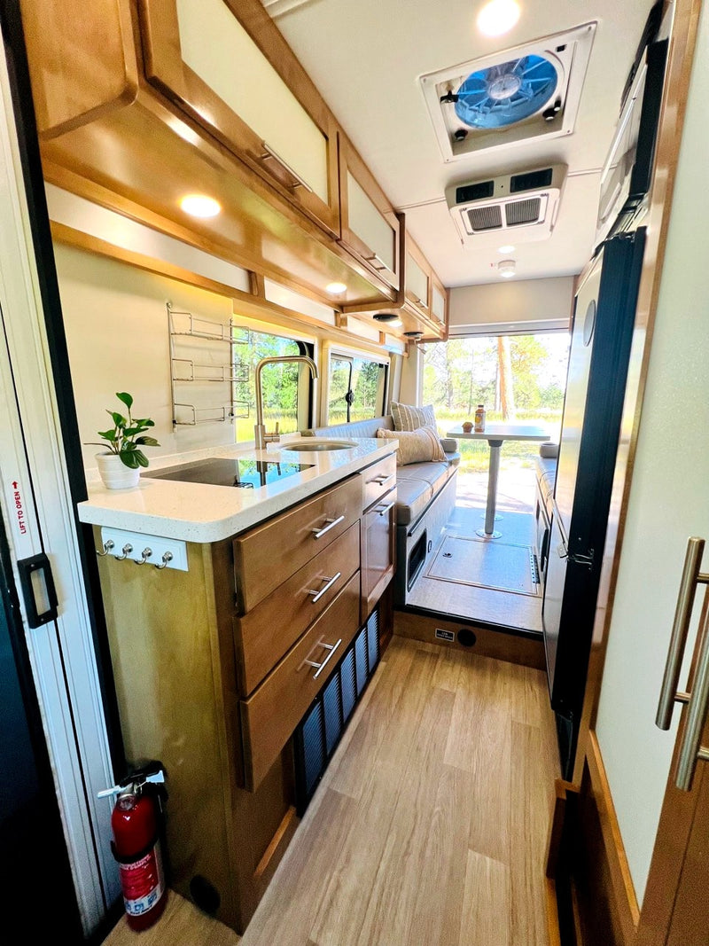 View inside an rv rental, showing a well-equipped kitchen with sink, compact dining area, and rear windows with nature views. — photo 8