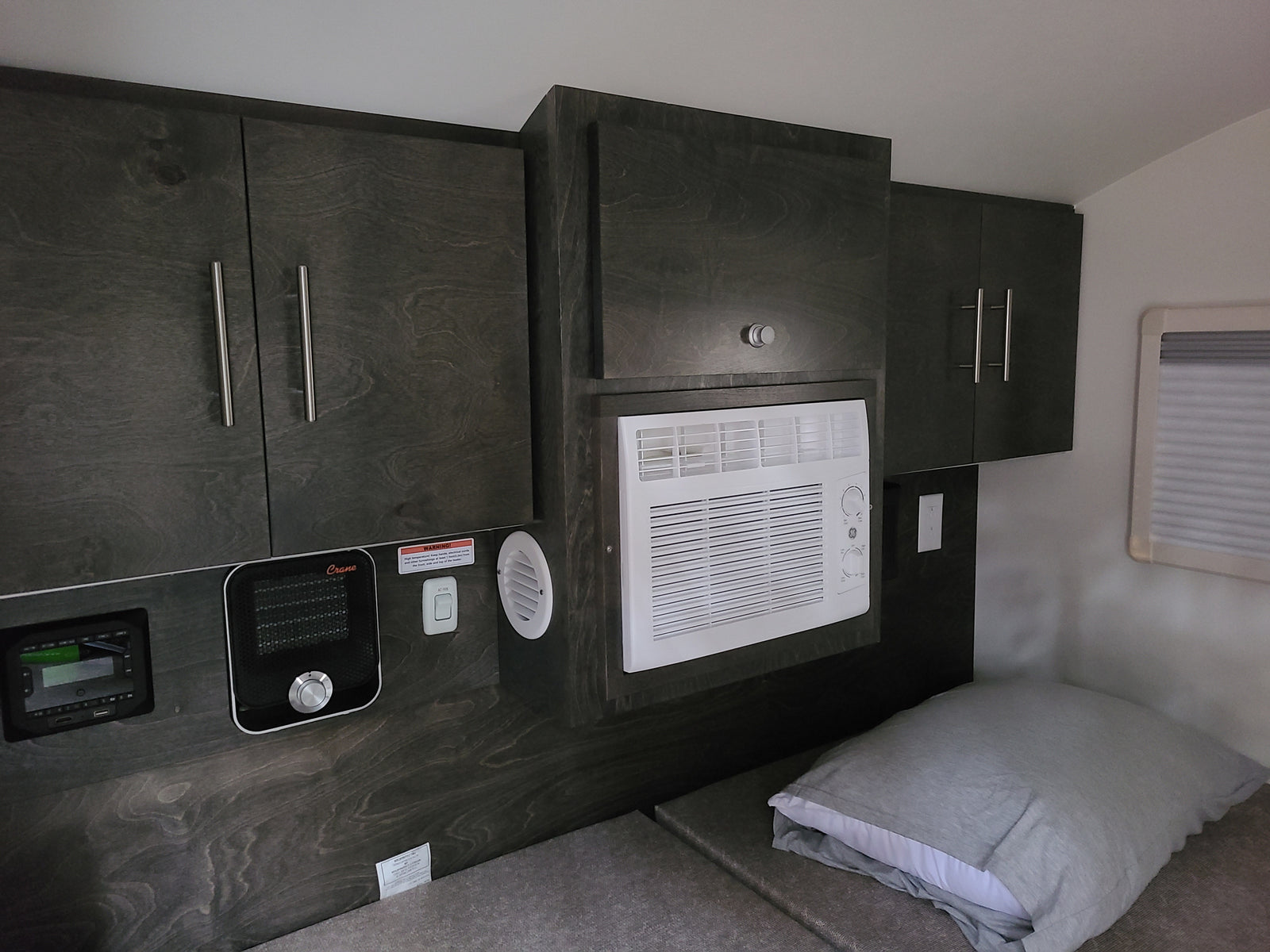 Compact RV rental interior featuring dark wood cabinets, AC, heater, and a comfy bed area.