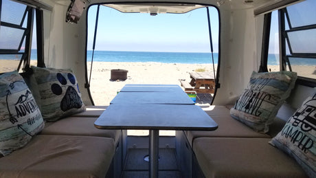 Relaxing inside an **RV rental** with an amazing beach view. Comfortable seating and a table offer a perfect **camping** setup by the **ocean**.
