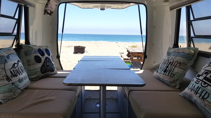 Relaxing inside an **RV rental** with an amazing beach view. Comfortable seating and a table offer a perfect **camping** setup by the **ocean**. — photo 14