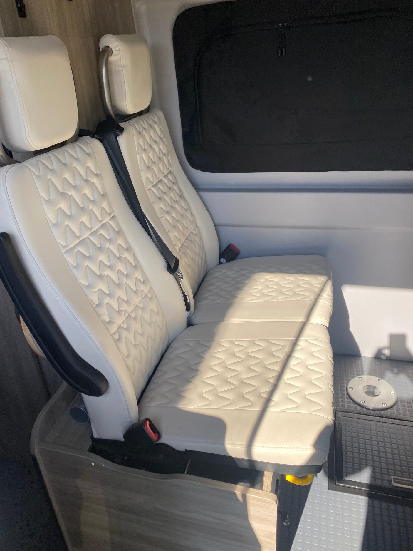 RV rental interior features white quilted passenger seats, a dark window, and a floor mount in a camper van.