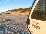 This RV rental, a Boondock Lite, on a sandy beach near dunes offers perfect outdoor camping and adventure.