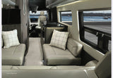 Experience luxury RV rental with this spacious, modern greige interior showing comfy seating, kitchen, and a scenic view of boats on the water.