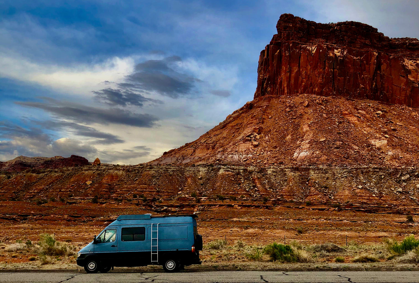 Explore stunning red rock landscapes with a blue RV rental parked beside towering mesas under a dramatic sky.