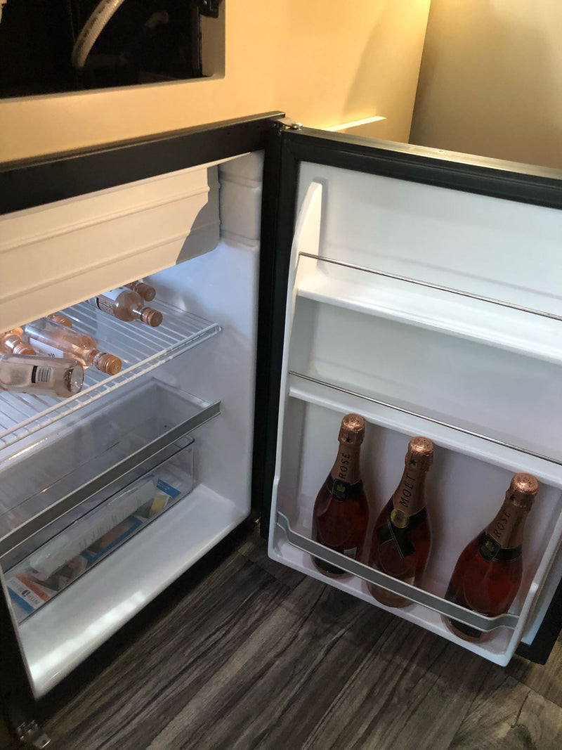 An open RV rental mini-fridge showing rosé wine bottles on shelves and champagne in the door. — photo 16