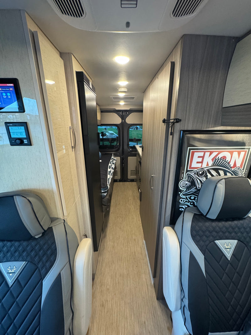 Looking down the narrow aisle of an RV rental, showing sleek grey seats, a refrigerator, and control panels. Ideal for a road trip. — photo 14