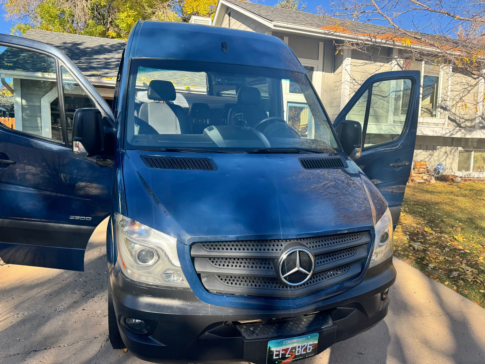 Blue Mercedes-Benz Sprinter camper van, ideal for your next rv rental. Doors open, parked on a sunny autumn day.