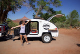 Happy woman with an RV rental teardrop camper in a desert. Perfect for outdoor camping and travel adventures.