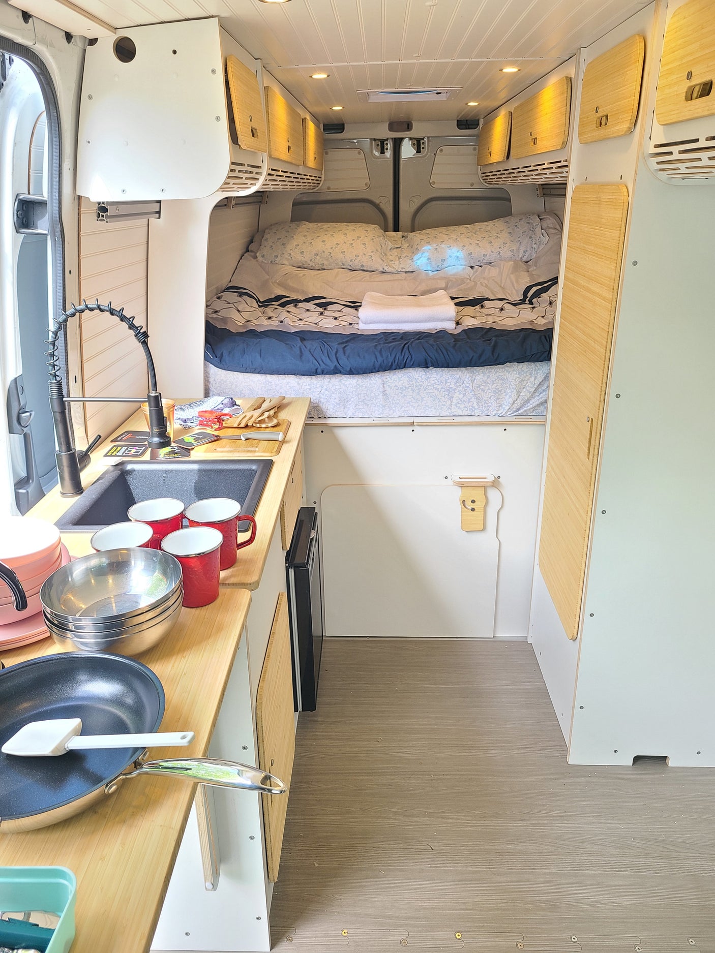 Spacious RV rental interior featuring a well-equipped kitchen with sink and cookware, a comfortable bed, and overhead storage.