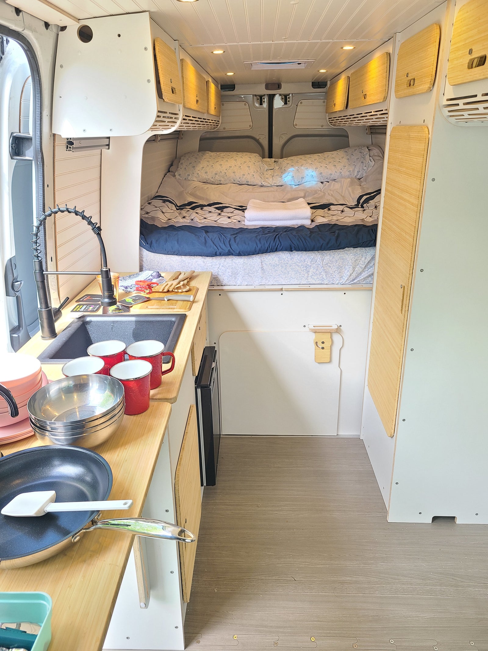 Spacious RV rental interior featuring a well-equipped kitchen with sink and cookware, a comfortable bed, and overhead storage.