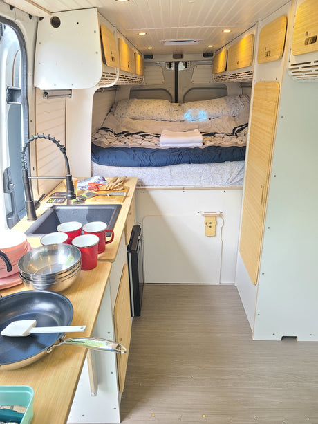 Spacious RV rental interior featuring a well-equipped kitchen with sink and cookware, a comfortable bed, and overhead storage.