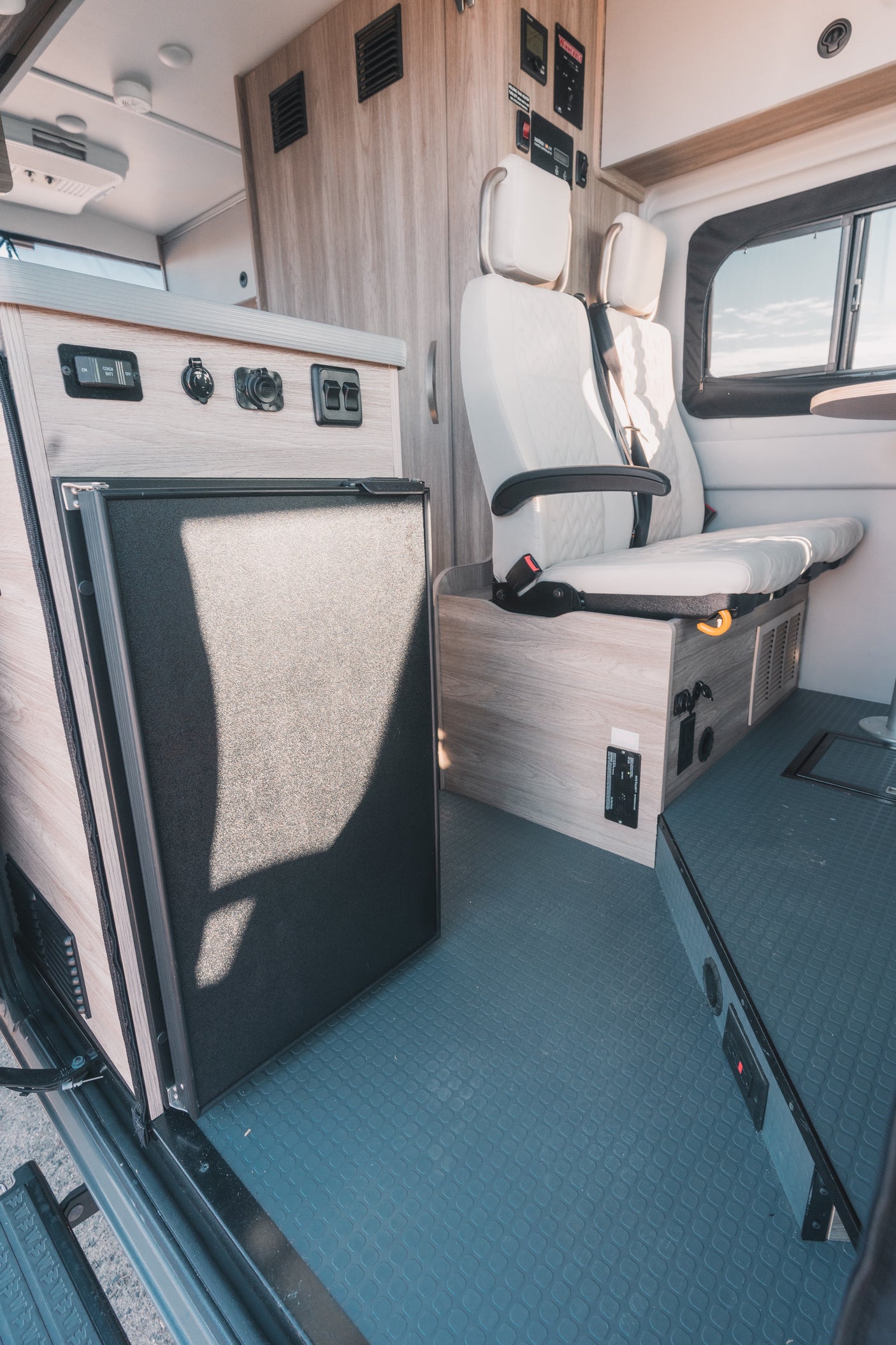 This RV rental interior features a built-in fridge, comfy seating, and control panel, ready for your adventure.