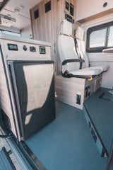 This RV rental interior features a built-in fridge, comfy seating, and control panel, ready for your adventure.