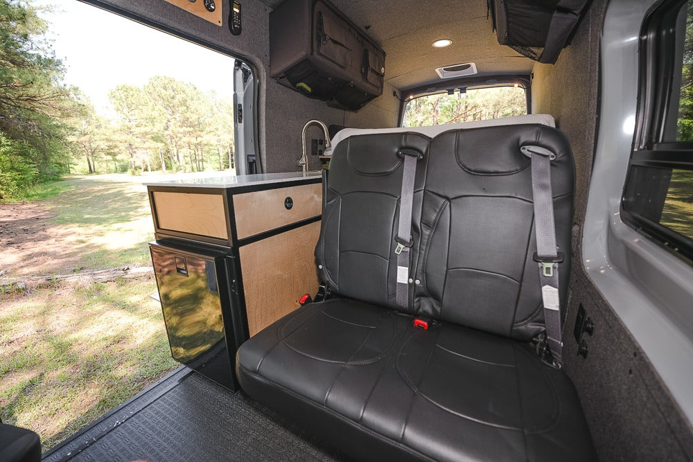 Camper van interior for RV rental: comfy seats, kitchen, fridge, and nature view through the open door.