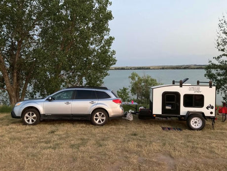 Outdoor adventure: A silver Subaru Outback and a white compact rv rental camper parked by a lake.