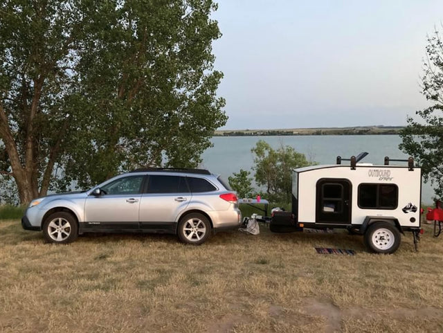 Outdoor adventure: A silver Subaru Outback and a white compact rv rental camper parked by a lake.