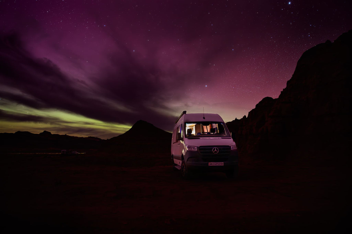 An RV rental illuminated against a vivid purple and green aurora, revealing stars and distant mountains. Perfect for night adventures.