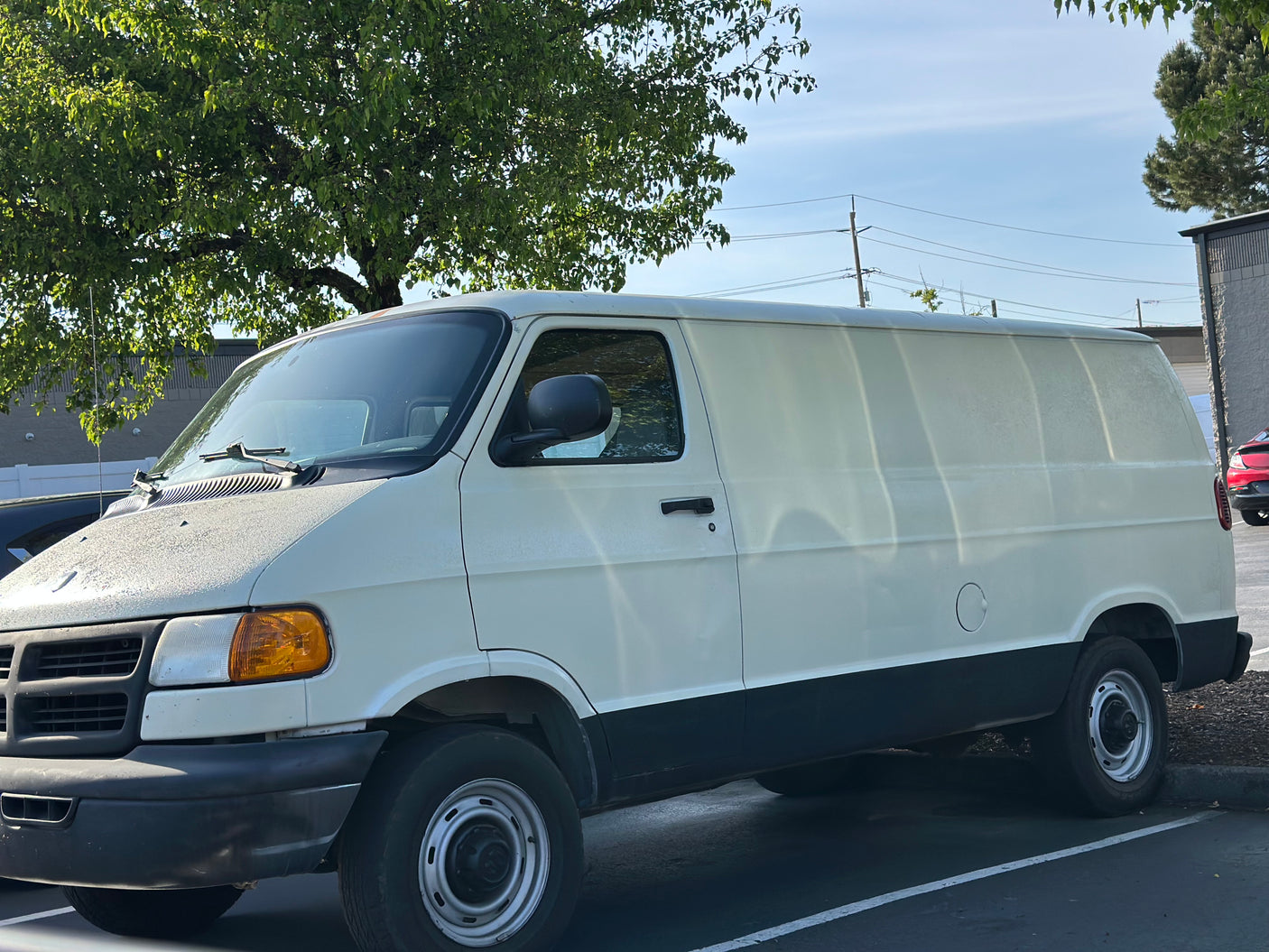 A white and black Dodge Ram cargo van, often customized for RV rental, parked in a lot on a sunny day.