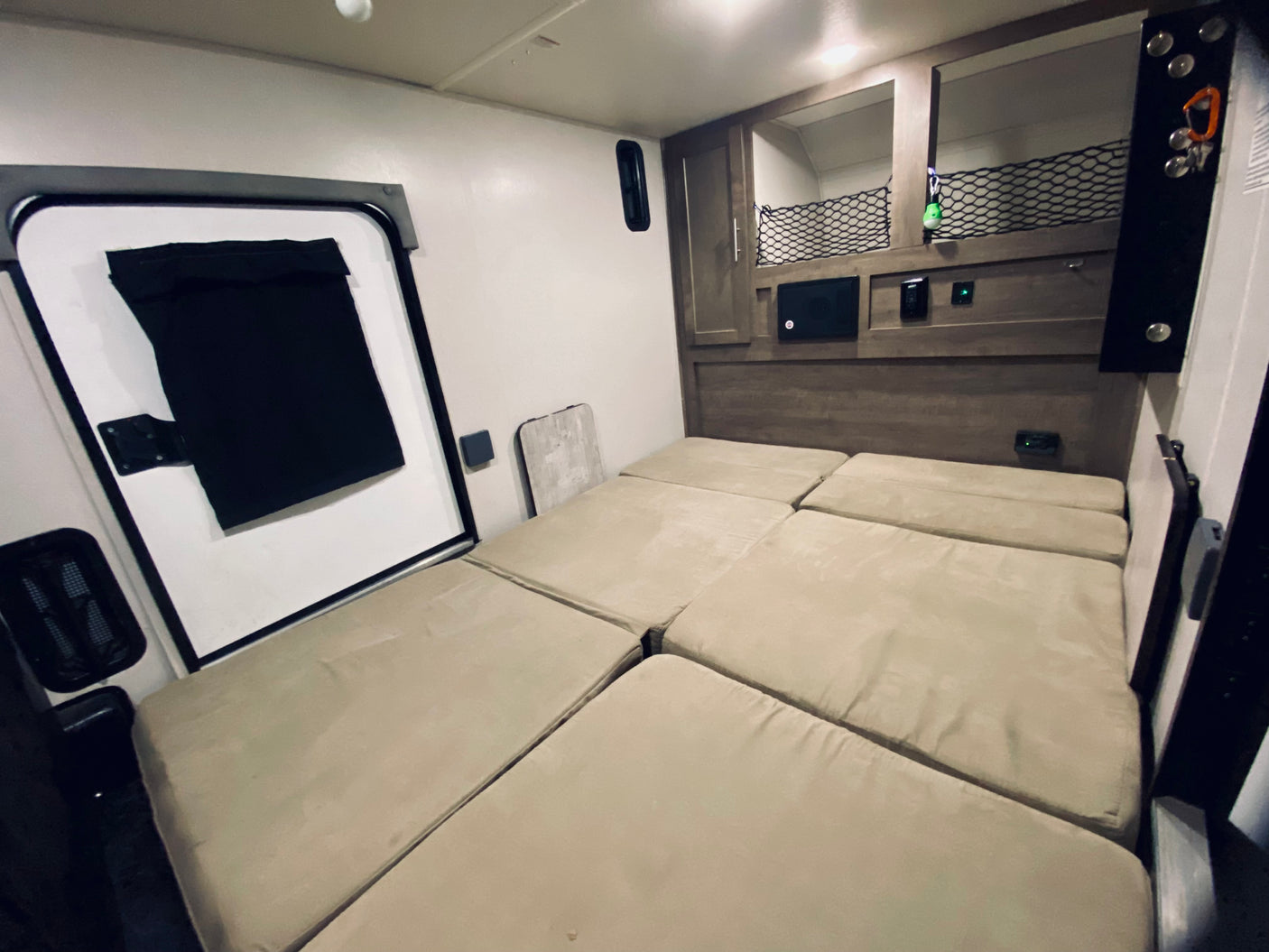 RV rental interior: Light-colored modular bed, black-framed door, and built-in wood storage with netting.