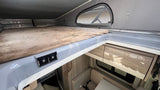 Inside an RV rental, showing the comfy pop-top bed with USB ports above the lower living area and cabinets.