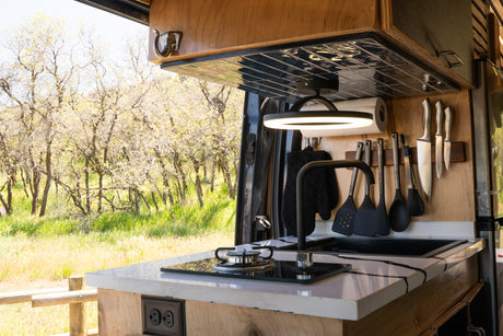 RV rental kitchen: compact stove, sink, and utensils, perfectly set against a vibrant outdoor nature view. Enjoy mobile cooking!