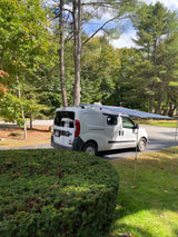White camper van with an extended awning, perfect for an RV rental adventure in nature.