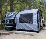RV rental setup: A modern teardrop camper with an attached tent extension at a wooded campsite, ideal for outdoor adventures.