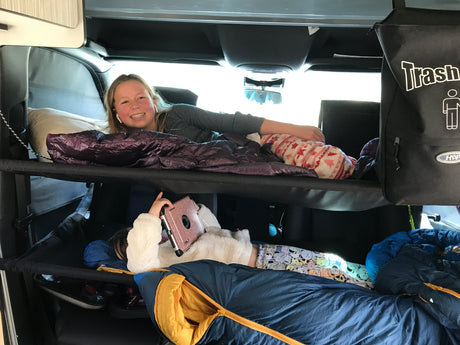 Two girls relaxing in bunk beds within an RV rental. Top girl smiles, bottom uses tablet. Ideal for road trip camping.
