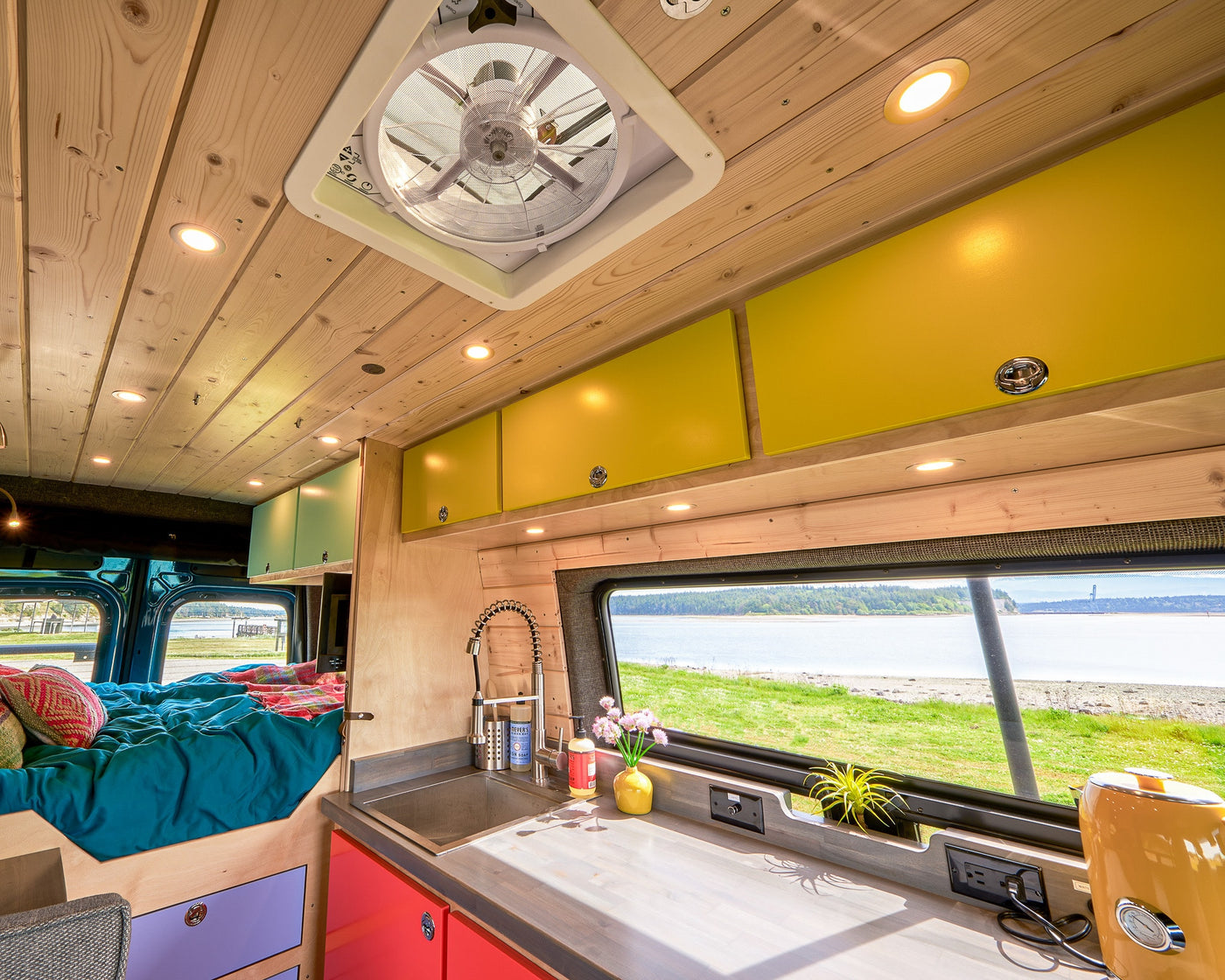 Experience comfort! This custom RV rental interior features a bright kitchen, cozy bed, and scenic coastal views. — photo 11