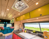 Experience comfort! This custom RV rental interior features a bright kitchen, cozy bed, and scenic coastal views.