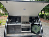 RV rental's compact rear kitchen with sink, stove, microwave, coffee maker, and cooler ready for outdoor adventures.