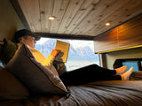 Relaxing with a book in a cozy rv rental, featuring stunning mountain views from inside the comfortable camper van.