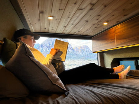 Relaxing with a book in a cozy rv rental, featuring stunning mountain views from inside the comfortable camper van.