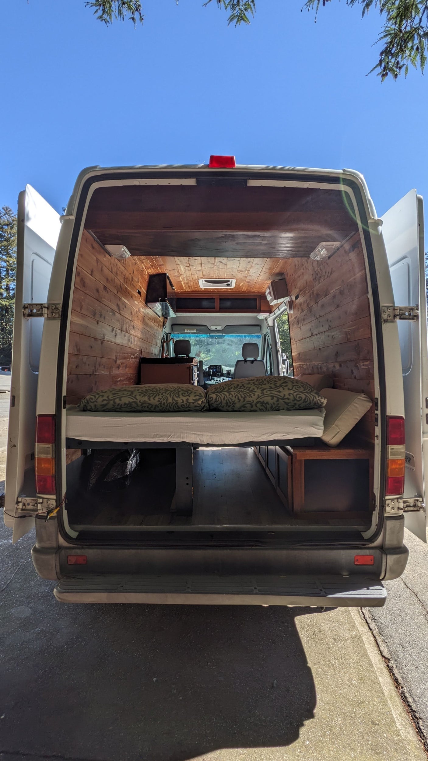 This RV rental showcases a bright, wood-paneled camper van interior with a comfortable bed, under-bed storage, and front cab view.