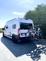 White Rove Vans camper, an RV rental, with two e-bikes on its rear rack, parked on a sunny day.