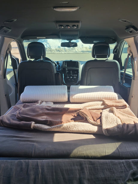 This cozy RV rental setup in a minivan features a comfy bed with pillows and blankets for road trips.