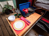 RV rental outdoor kitchen: A convenient pull-out setup with a two-burner stove, pot, pan, and dinnerware ready for camping adventures.