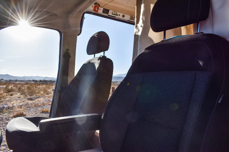 An RV rental interior, featuring front seats with a view of a sun-drenched desert, ideal for remote van life travel.