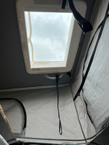 View inside an RV rental showing an open ceiling skylight with cloudy sky, and light grey pop-top walls.