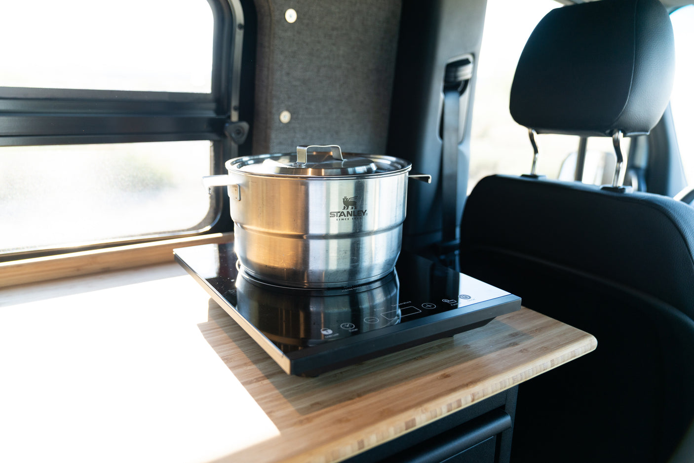 A stainless steel pot sits on an induction cooktop on a wooden counter in an RV rental, with a window nearby.