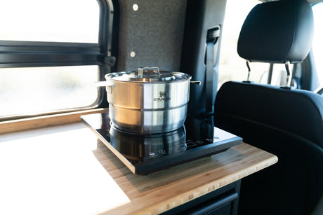 A stainless steel pot sits on an induction cooktop on a wooden counter in an RV rental, with a window nearby.