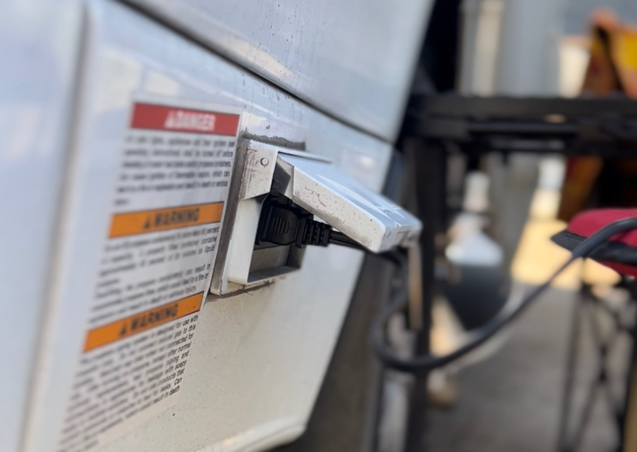 Close-up of an RV rental's exterior power outlet with a black cord plugged in, next to a safety warning.