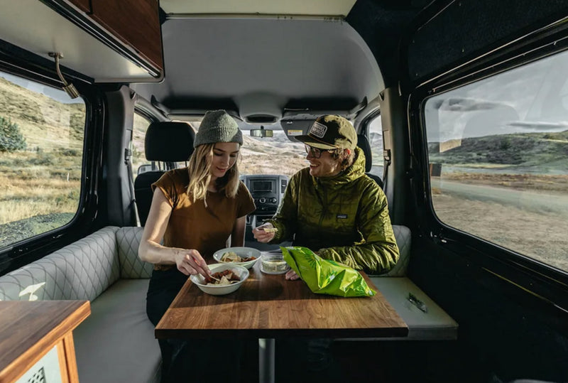  gazing at the vast desert through the open van doors.|An RV rental interior features a man accessing overhead storage. Kitchen with sink — photo 6