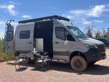 Grey Winnebago rv rental camper van parked with side door open, revealing outdoor table and chairs for a relaxing camp setup.