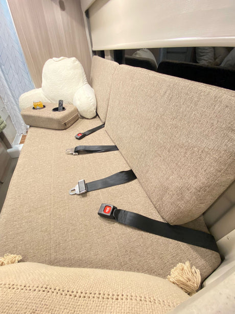 Cozy RV rental interior featuring a comfy bench seat with three safety belts, plus a leisure setup with a drink and remote.