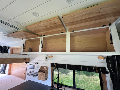 Bright, modern RV rental interior with open overhead wood cabinets, bed, and kitchen area for compact living.