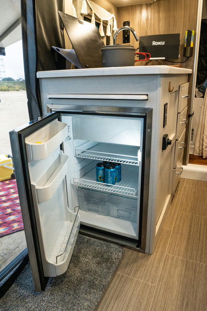 Inside an RV rental, a compact kitchen features an open fridge with drinks, sink, and Roku setup. Perfect for travel. — photo 12